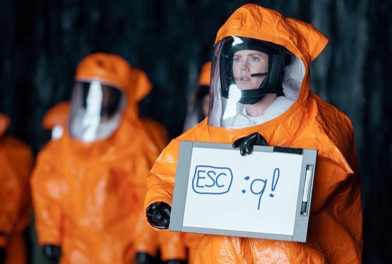 Amy Adams is holding a sign in an attempt to communicate with aliens in the film "Arrival", but instead of showing the word "Human" it shows the command to exit Vim